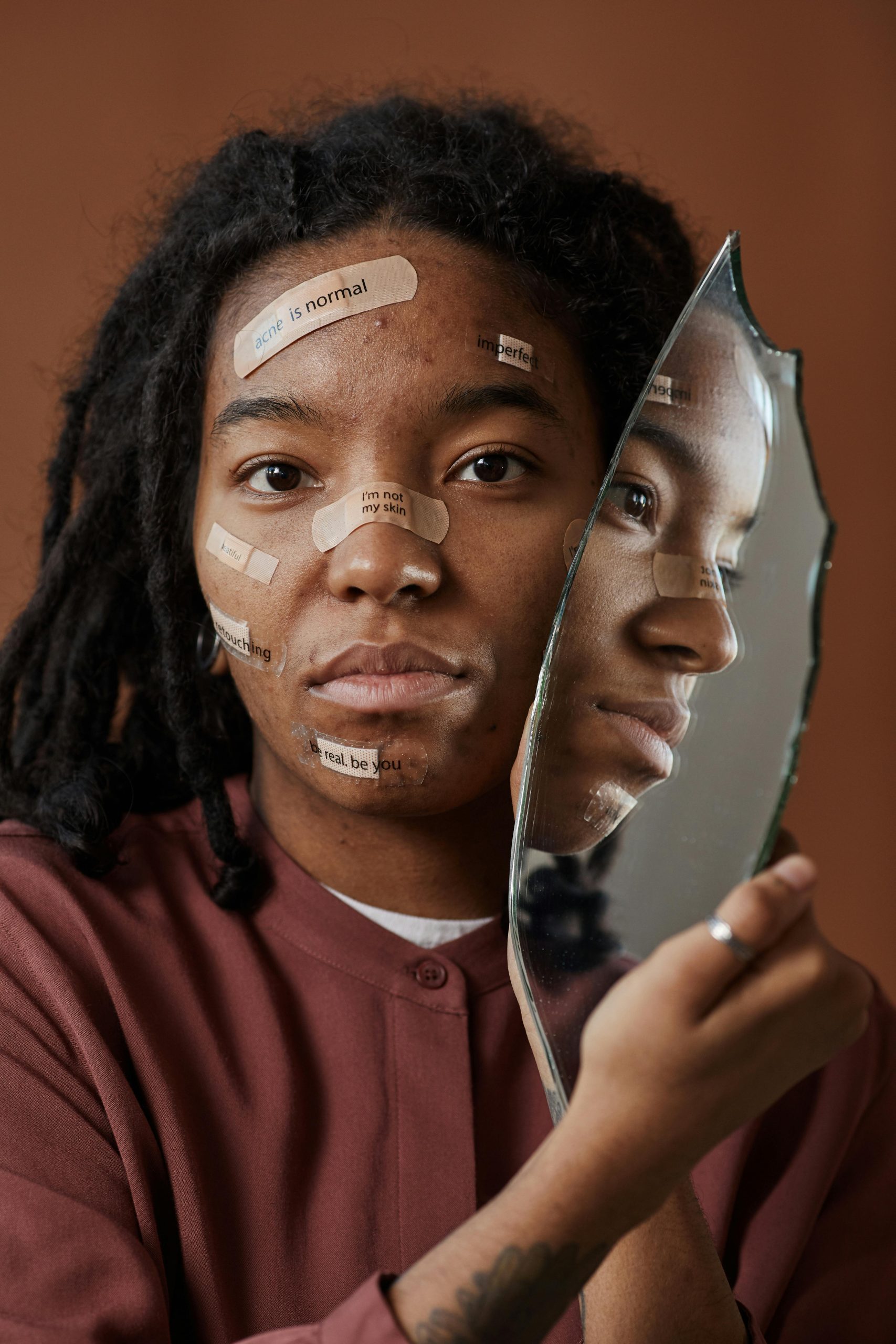 An African woman holds a broken mirror, surrounded by positive affirmations.